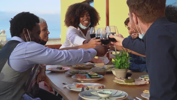 Young friends toasting with red wine glasses at dinner appetizer during sunset time