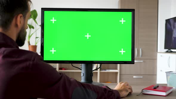 Side View of Man Sitting in Front of Computer with Big Green Screen Mock-up Chroma Typing on the