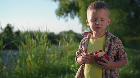 Portrait of a Vegetarian Child with Pleasure and Pleasure Eating a Ripe Organic Apple While Walking