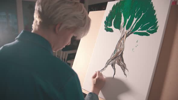 A Young Blonde Woman Artist Painting a Tree Root in Darker Color