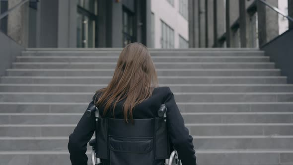 Backside View of Brunette Female Person in Suit on Wheel Chair at City Street