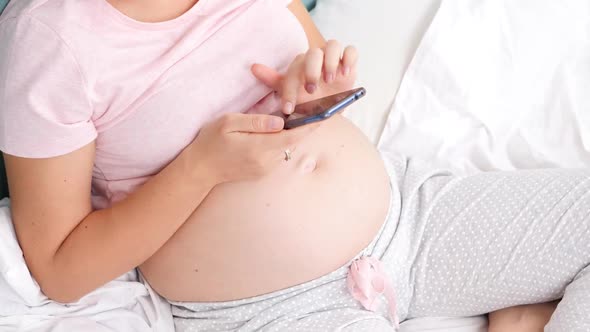 Top View Shot of Young Pregnant Woman with Big Belly Browsing Internet and Using Smartphone