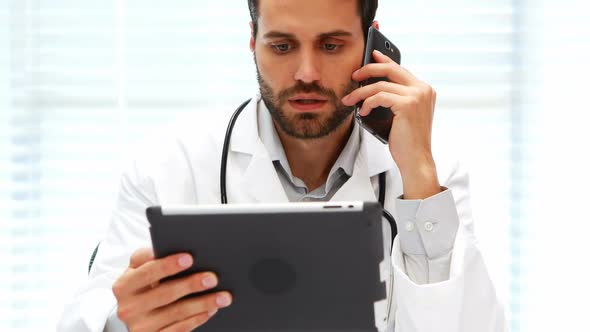 Male doctor talking on mobile phone while using digital tablet