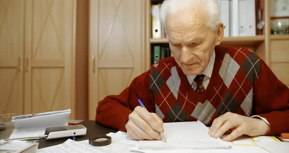 Senior Businessman Writing on Paper at Table in Office