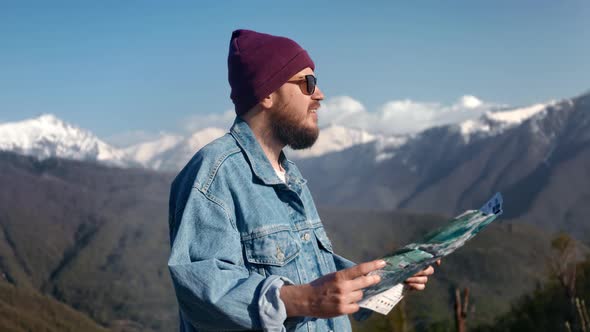 Attractive Traveller Man Hiker with Backpack Checking Map to Find Direction in the Mountains