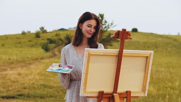 Young Smiling Woman Drawing a Painting on Nature Standing on the Field