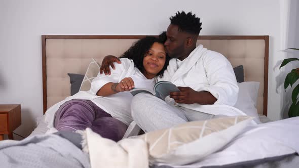 Wide Shot Loving Husband Kissing Wife Enjoying Reading with Pregnant Spouse Lying in Bed
