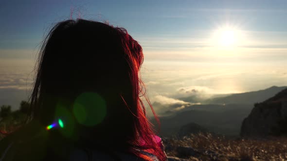 Young Redhead Woman in Sunglases Sitting on a Rock High in the Mountains Above the Clouds and