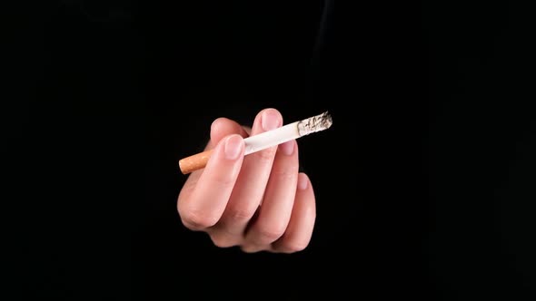 hand with smoking cigarette emerges from darkness, inviting the viewer to smoke