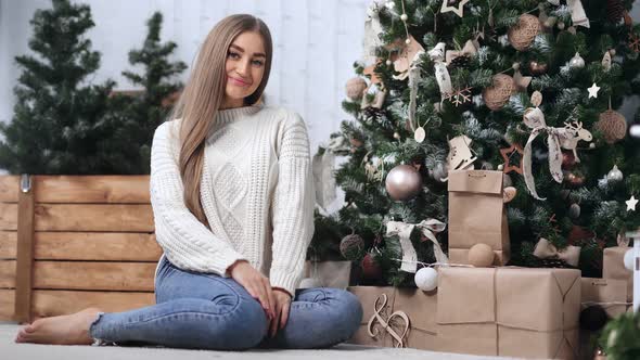 Beautiful Cozy Girl in Casual Clothing Sitting Near Decorate Christmas Tree