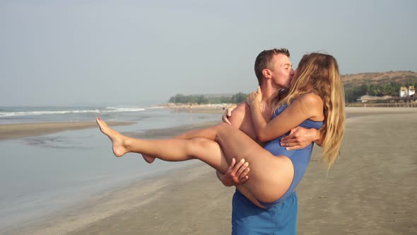 A Young Couple in Love, a Man Carries a Woman in His Arms Along the Beach