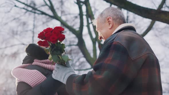 Elderly Man Giving Red Roses To Elderly Woman in the Park in Winter