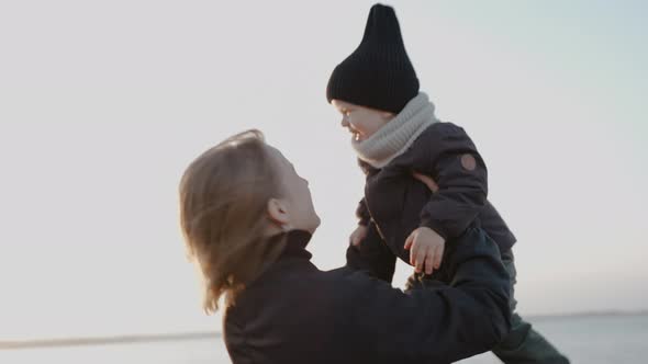 Happy Woman Raises Her Child to the Sky on the Shore of Lake on a Fall Evening