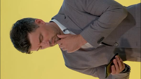 Tall Man in Suit Holding One Hand on Chin, Looking on Smartphone and Thinking About Something.