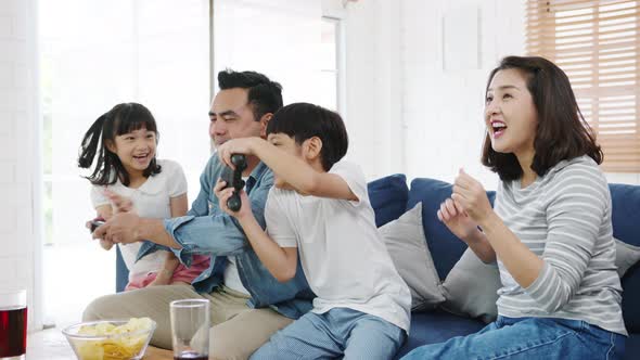 Happy Asian family funny playing video game with technology console on sofa in living room at house.