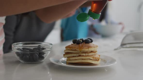 Midsection of girl in kitchen, putting syrup on stack of pancakes