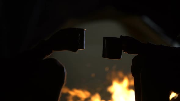 Iron Cups With Drinks Against Bonfire and Tent, Clinking Together, Close Up