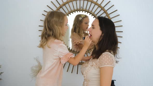 Little Girl Painting Lips of Her Mother Indoors