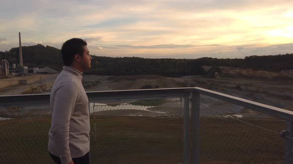 A young man in an turtleneck sweater looking over the quarry while the sun is setting