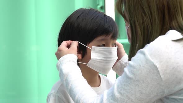 Asian Mother Puts A Safety Mask On Her Son Face