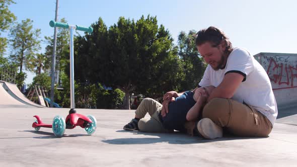 Little Boy with His Father Sitting on the Ground in the Skate Park