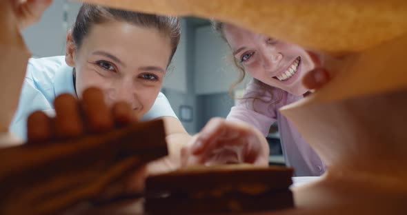 View From Inside Paper Bag of Smiling Female Colleagues Take Sandwich and Bite