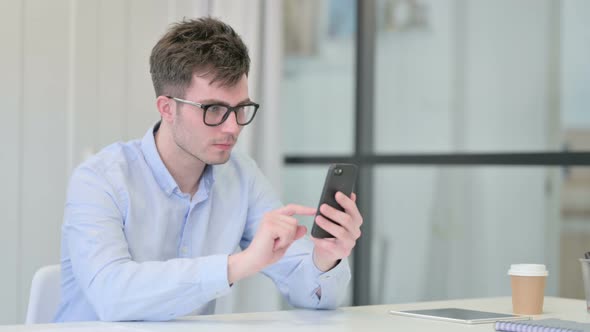 Young Man Reacting to Loss on Smartphone in Office