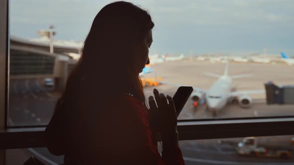 Businesswoman at Airport with Phone in Hands Against the Large Panoramic Window with Parking