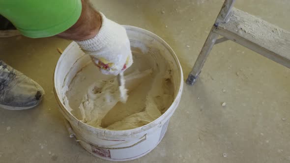 A man's gloved hand with a trowel stirring plaster in a bucket