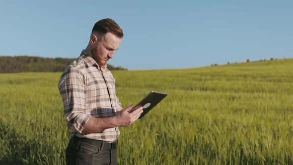 The Farmer is Standing Near the Field and Working with a Tablet