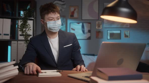 Young Asian Man Wearing Medical Mask Working Remotely at Home Typing on Laptop Computer During