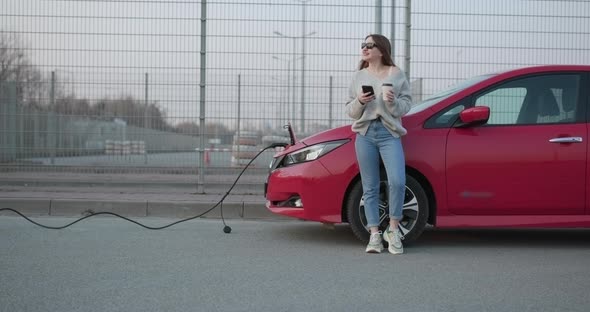 Girl Use Coffee Drink While Using SmartPhone and Waiting Power Supply Connect to Electric Vehicles