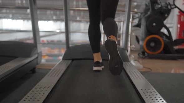 Closeup of Female Legs in Black Sneakers and Black Leggings on a Treadmill in the Gym
