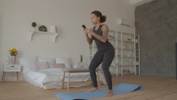 African American Woman with Phone Squats at Home