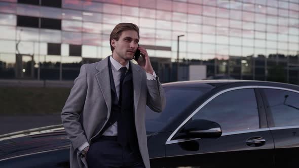 Young Businessman Standing Near a Business Car and Talking on a Mobile Phone Top Manager in a Suit
