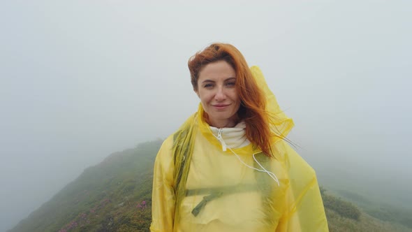 Portrait of a tired but content woman in yellow rain coat reaching the top of mountains in a bad wea