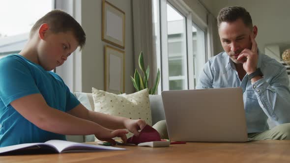 Caucasian father with son sitting at table and learning with laptop at home