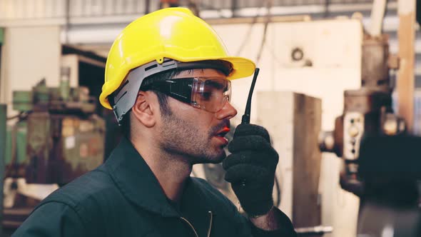 Factory Worker Talking on Portable Radio While Inspecting Machinery Parts