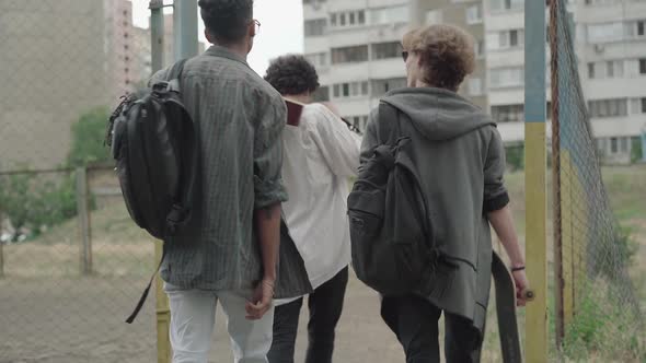 Back View of Three Young Boys Dressed in 1980s Style Entering Outdoor Sport Court. Camera Follows