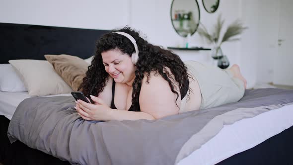 Young Overweight Brunette Lies on Bed Typing on Phone