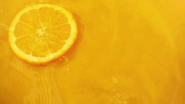 Orange slices fall into the water on an orange background. Slow motion.