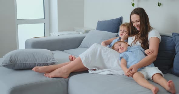 Children Hug Mom Sitting on the Couch and Watching TV
