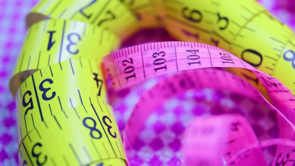 Close Up of a Pink and Yellow Measure Tape on Colored Rotating Background