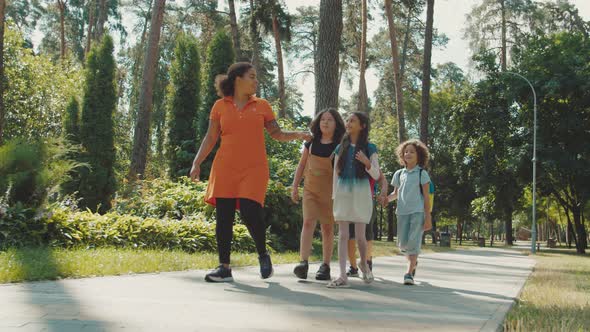 Young Female Teacher Coming Along Elementary Students in Public Park