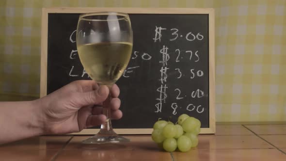 Hand with glass of white wine and grapes in cafe medium shot