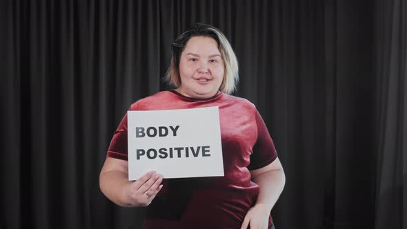 A Confident Flirty Overweight Woman Holding a Nameplate with a Sign BODY POSITIVE