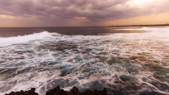 TimeLapse - Waves rolling in during sunset with motion blur, moody clouds in sky.