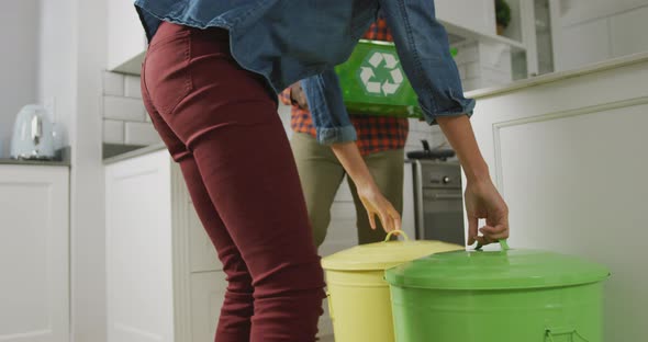 Diverse couple wearing shirt and jacket segregating waste in kitchen