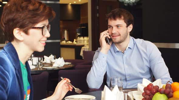 Pleasant Couple Having Lunch and Making a Phone Call at Cafe