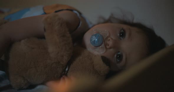 Little girl sleeping hugging her teddy bear with a pacifier in her mouth